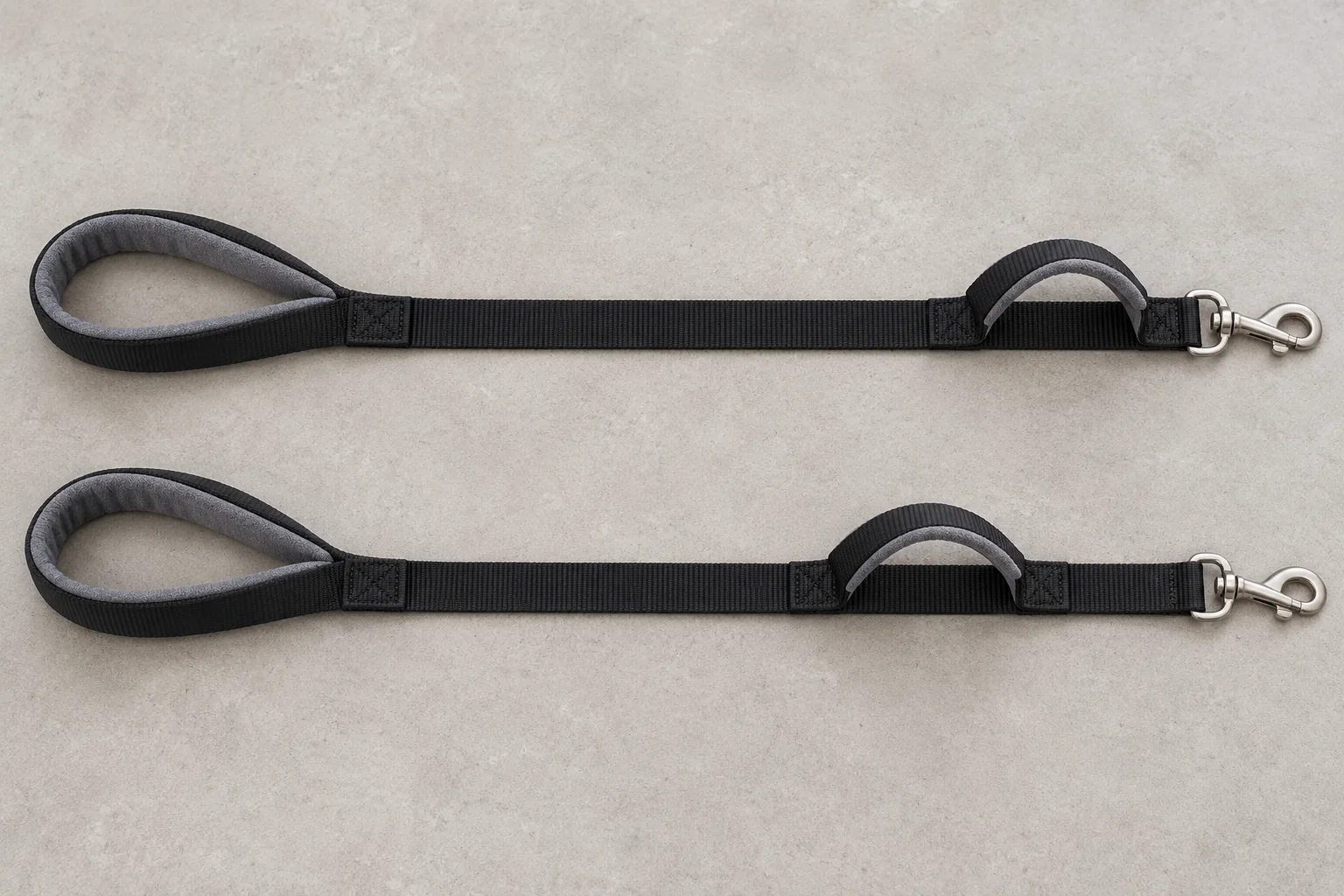 Two black leashes arranged in parallel with traffic handles positioned at different distances from the clips.