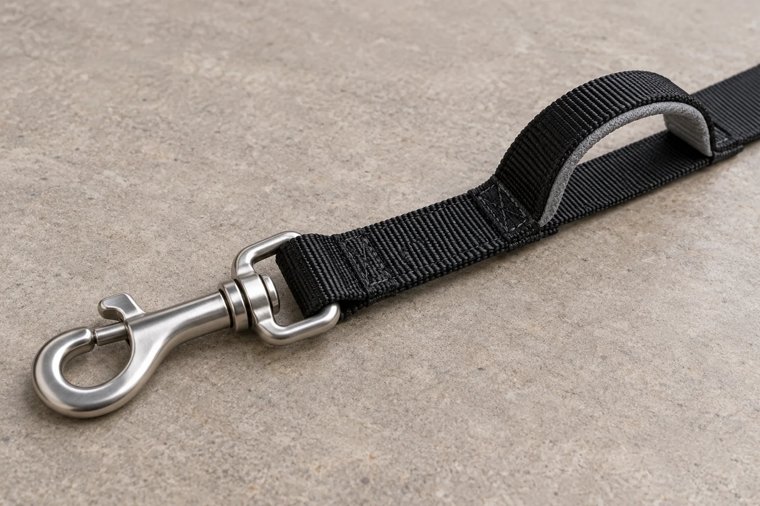 Silver swivel snap hook attached to folded black webbing beside a grey-lined traffic handle.